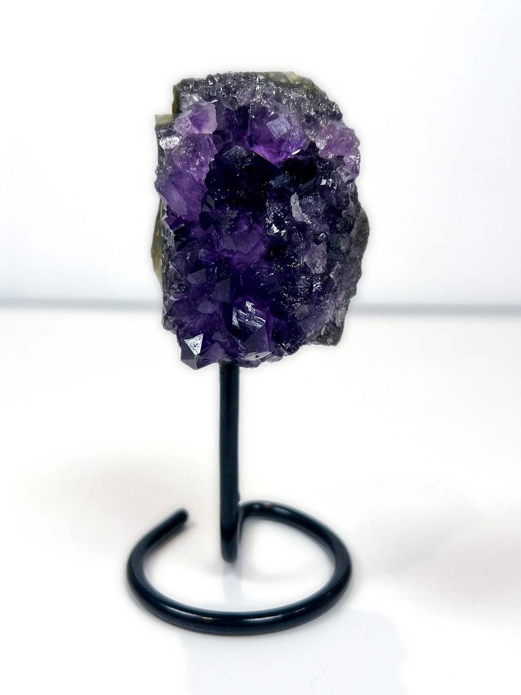 Amethyst crystal on a black stand against a white background