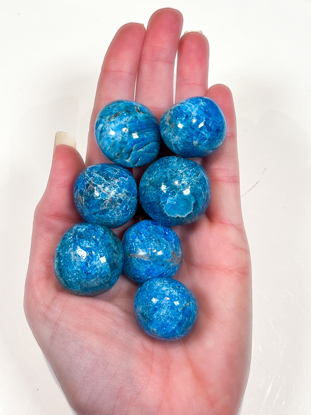 Hand holding a blue Apatite crystal on a white background.