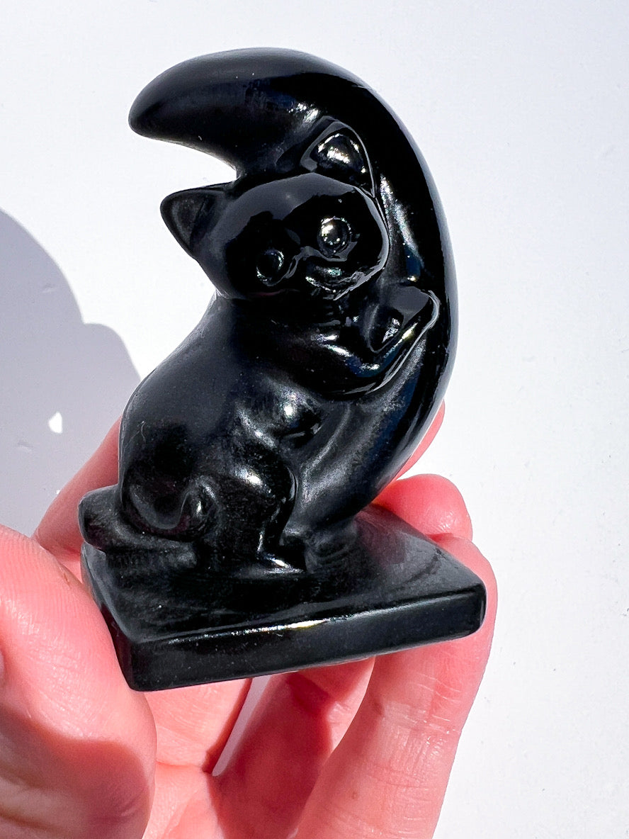 Black cat figurine on a crescent moon held in hand against a white background
