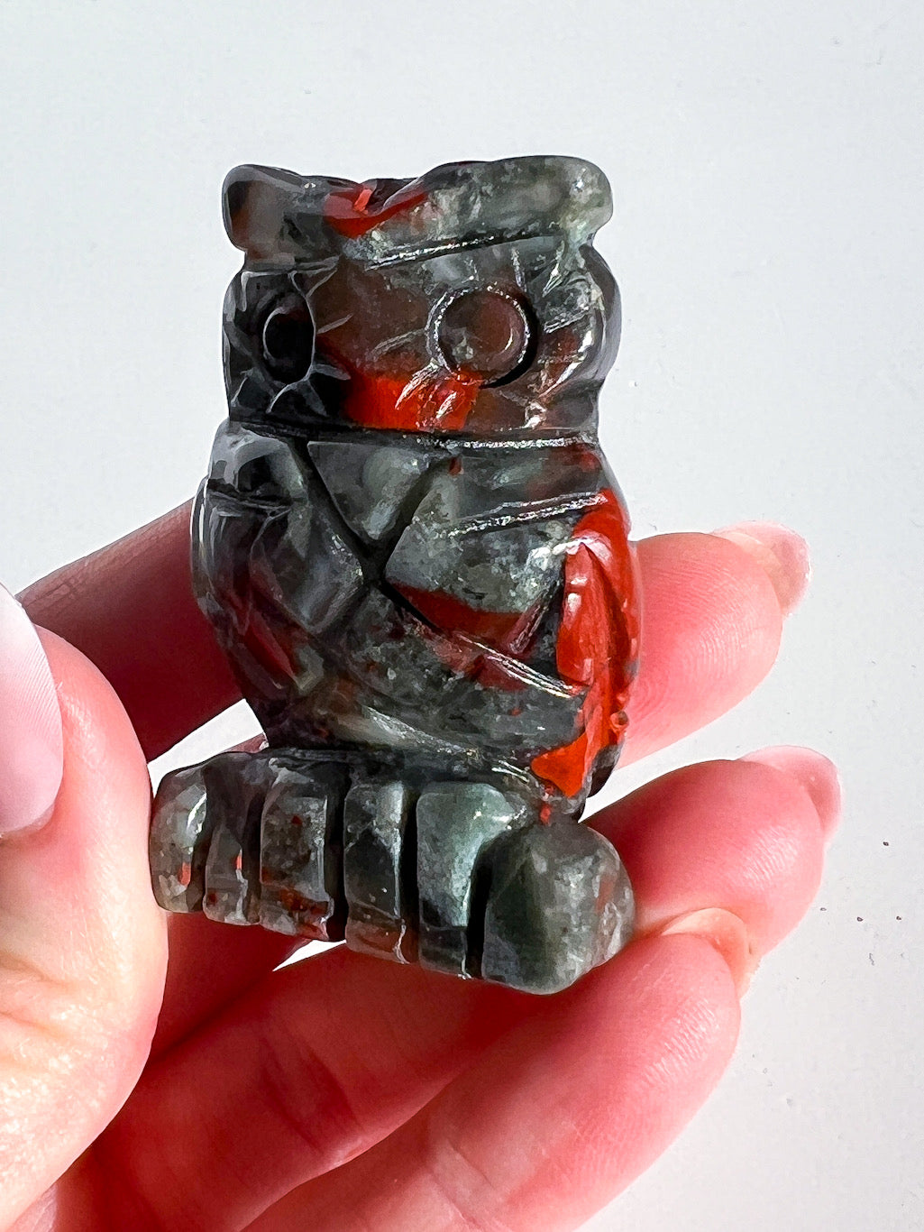Carved stone owl figure held in a hand against a white background