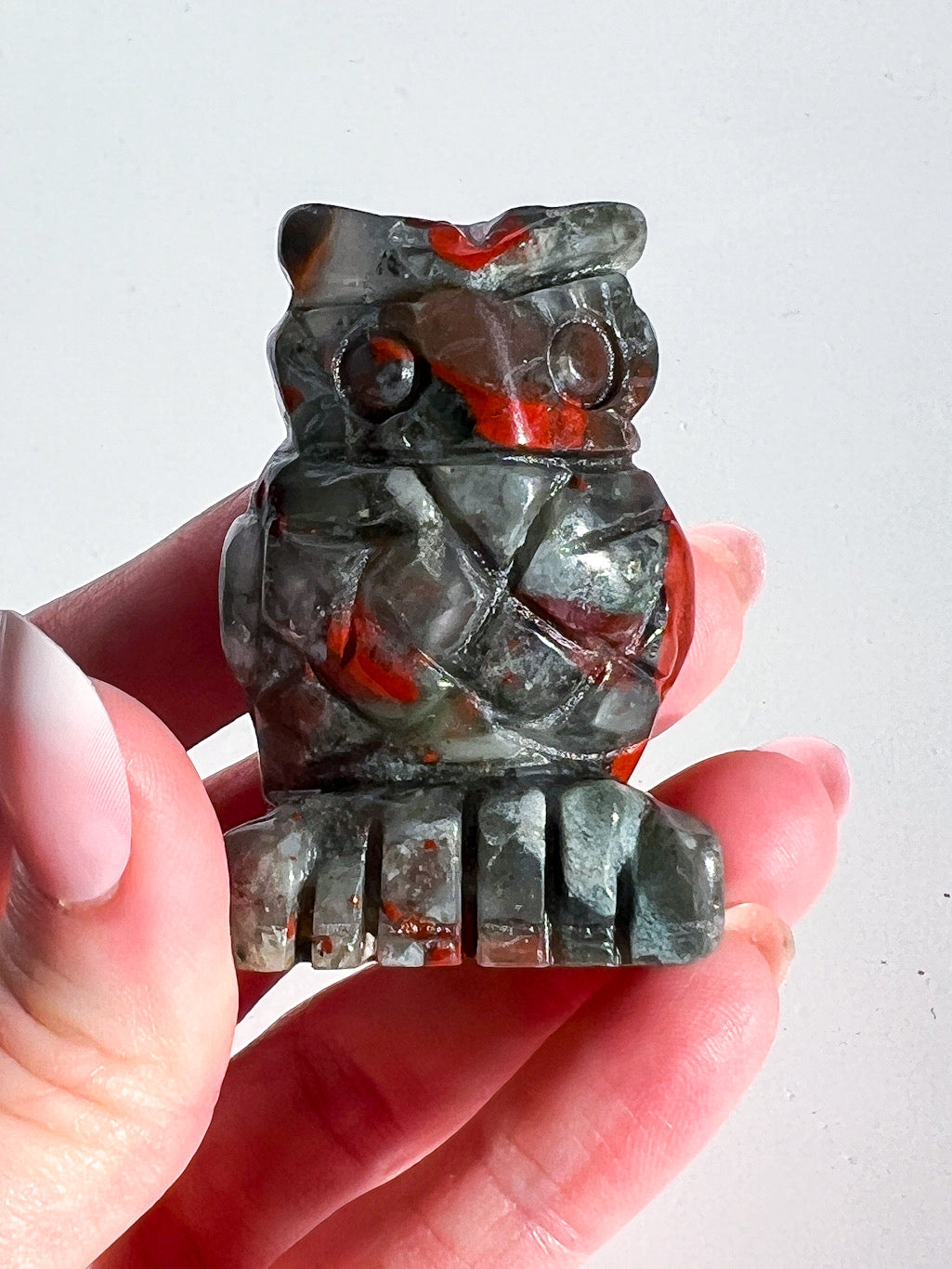 Hand holding a small stone owl figurine against a white background