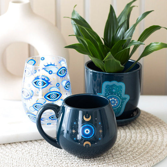 Celestial Protective Eye Mug on dinner mat with a glass and plant next to it.