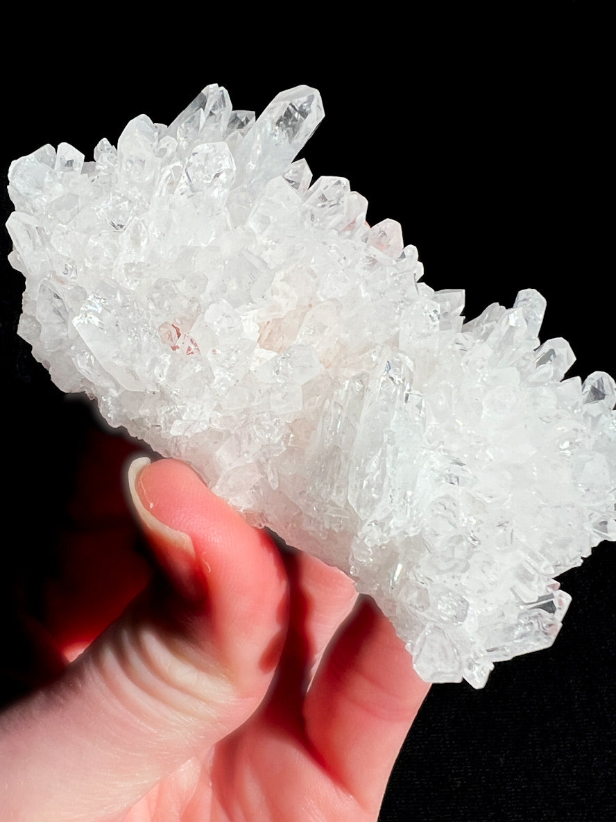 Hand holding a large crystal cluster against a black background