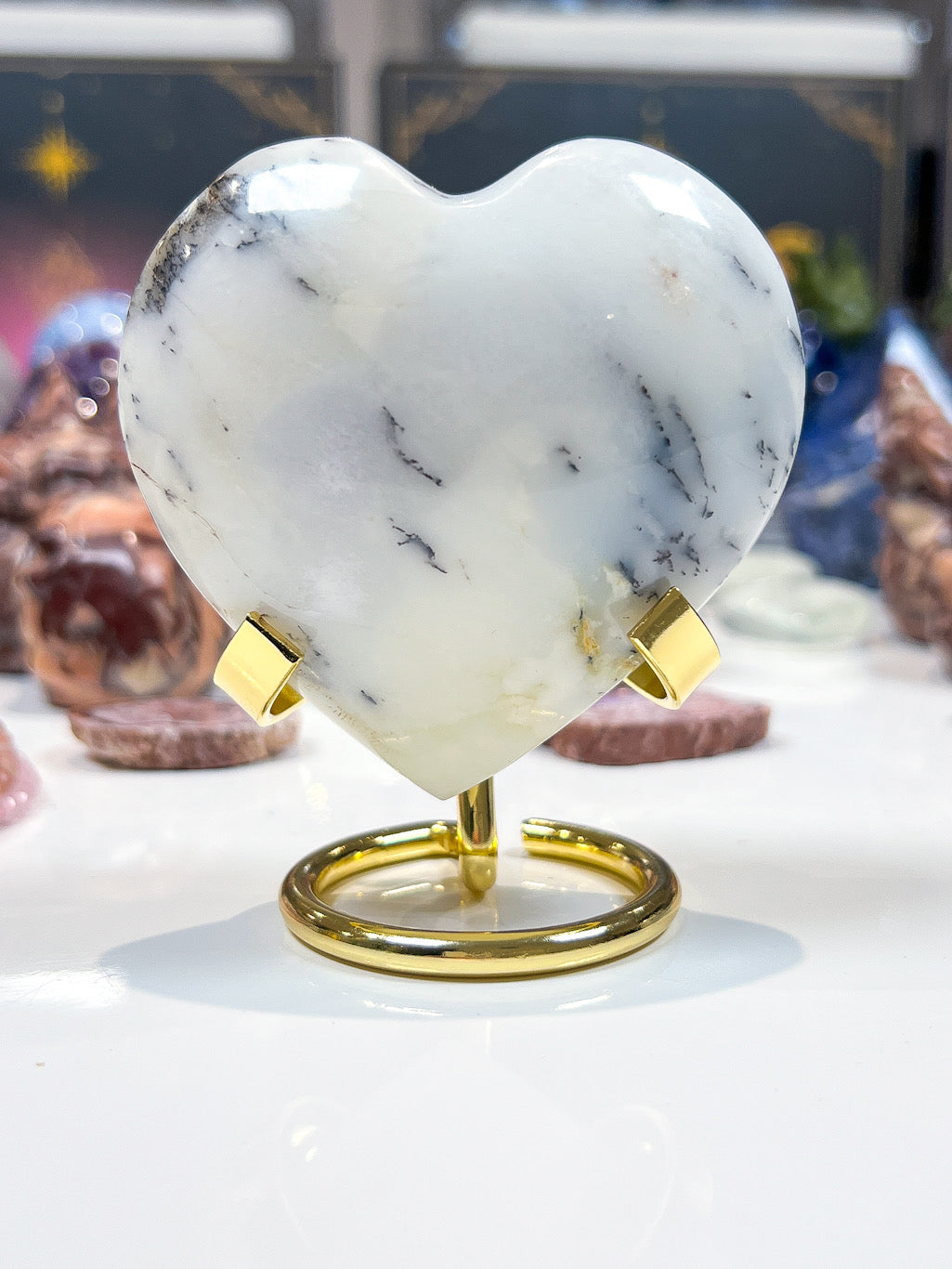 Marble heart-shaped object on a gold stand with blurred gemstones in the background