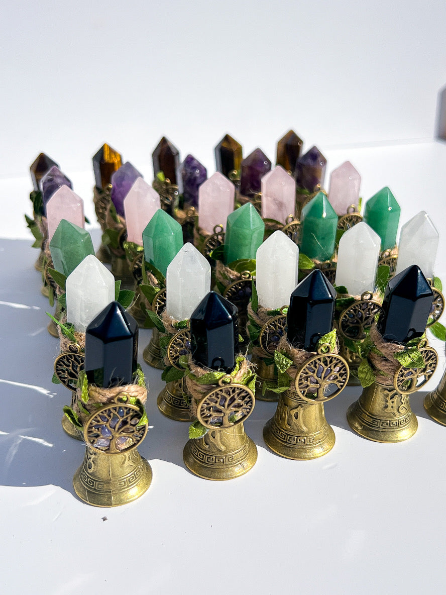 A collection of crystal point towers on brass stands, featuring various colored gemstones including green, white, pink, purple, and black, arranged on a white surface.