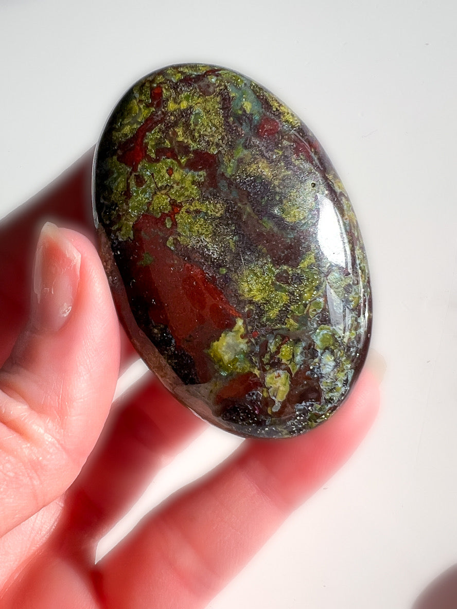 Dragon Bloodstone Palm Stone in a hand with white background