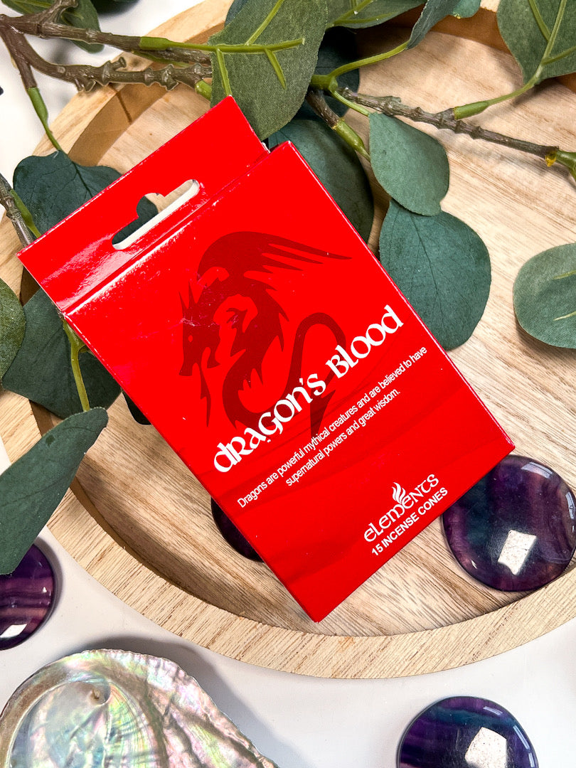 Red package labeled 'Dragon's Blood' on a wooden surface with green leaves and stones.
