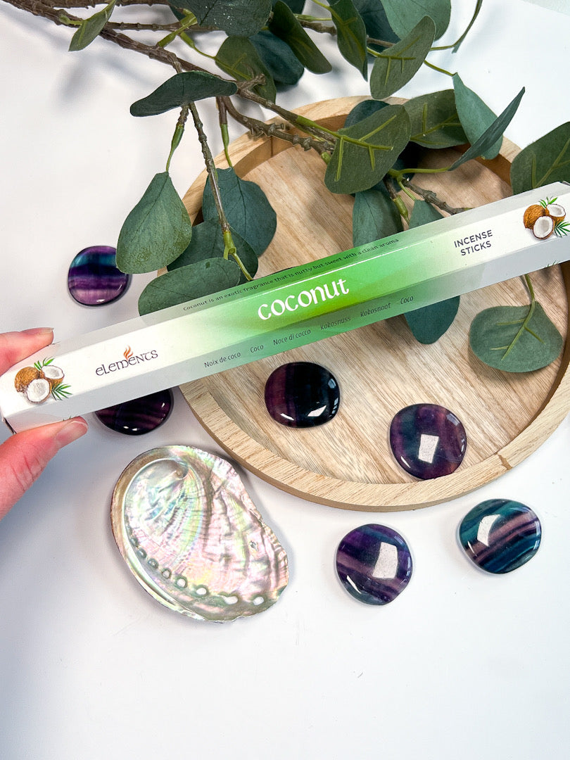 Elements coconut incense stick packaging held over a decorative setting with stones and leaves.