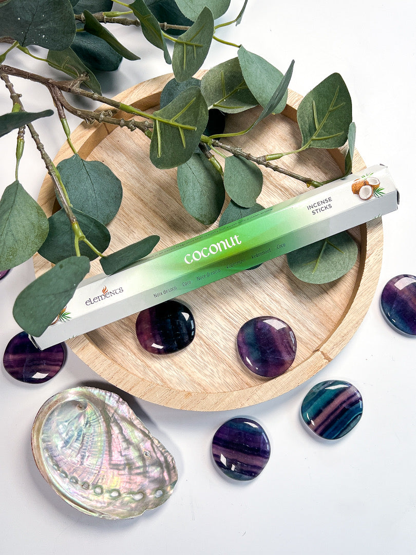 Coconut product with green gradient on a wooden tray with eucalyptus leaves and purple stones.