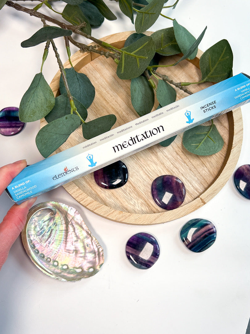 Meditation product with a wooden coaster, leaves, and stones on a white background