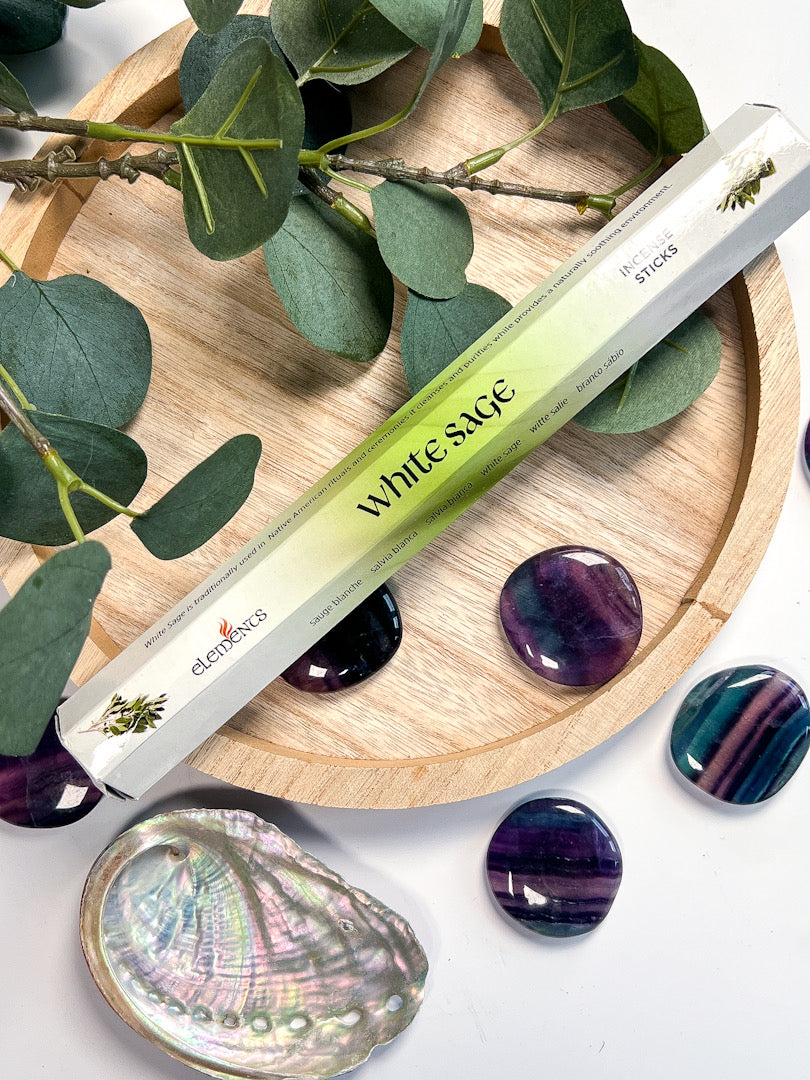 White sage stick on a wooden tray with green leaves and purple stones