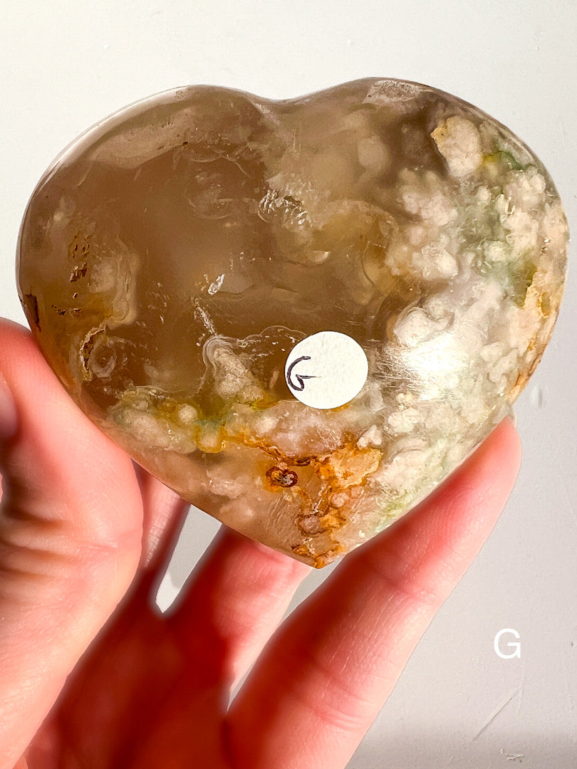 Heart-shaped crystal held in a hand with a visible brand logo on a white background