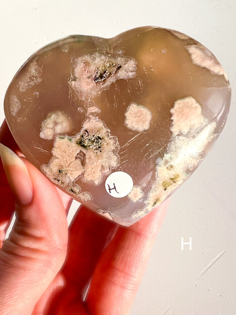 Heart-shaped crystal with visible inclusions held by a hand on a light background