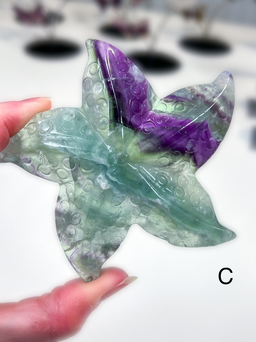 Decorative starfish made of green and purple material held by a hand on a white surface.