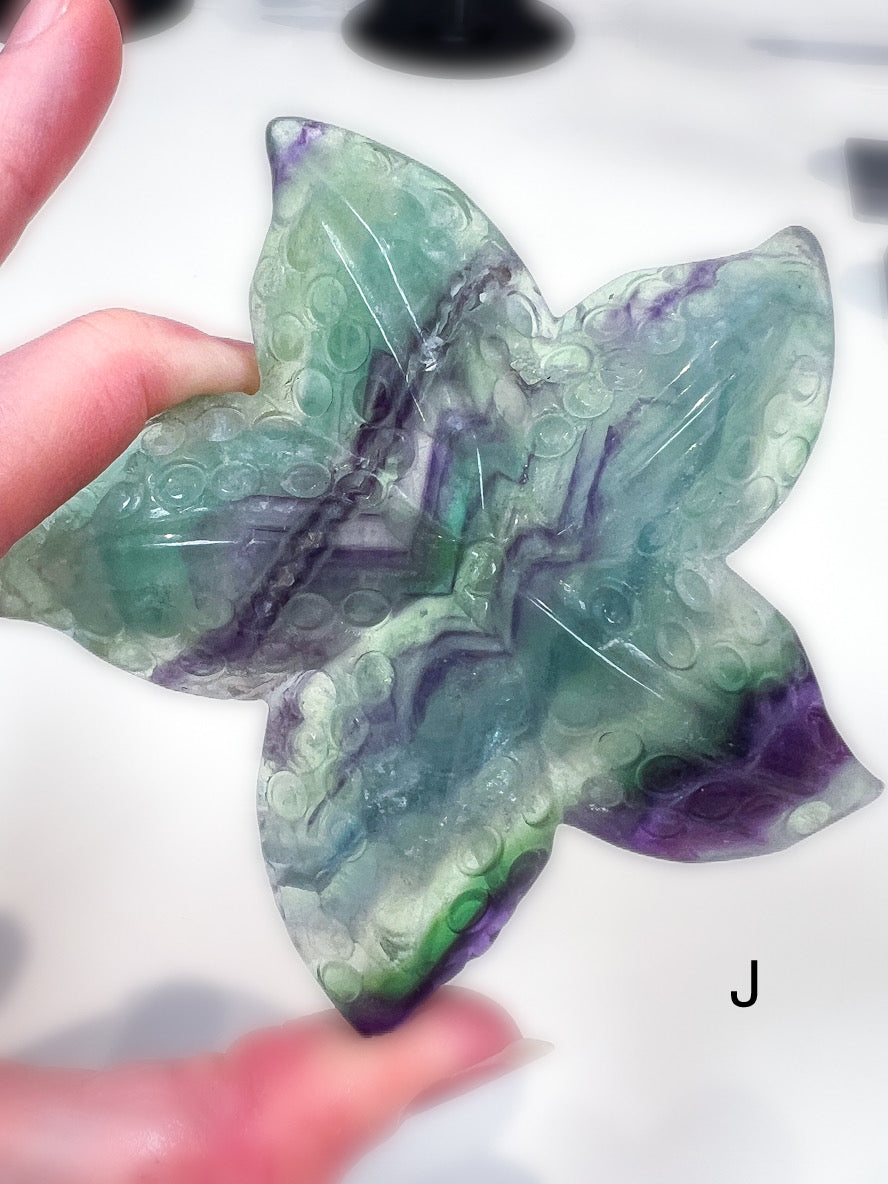 Starfish-shaped green and purple stone held by a hand on a white background