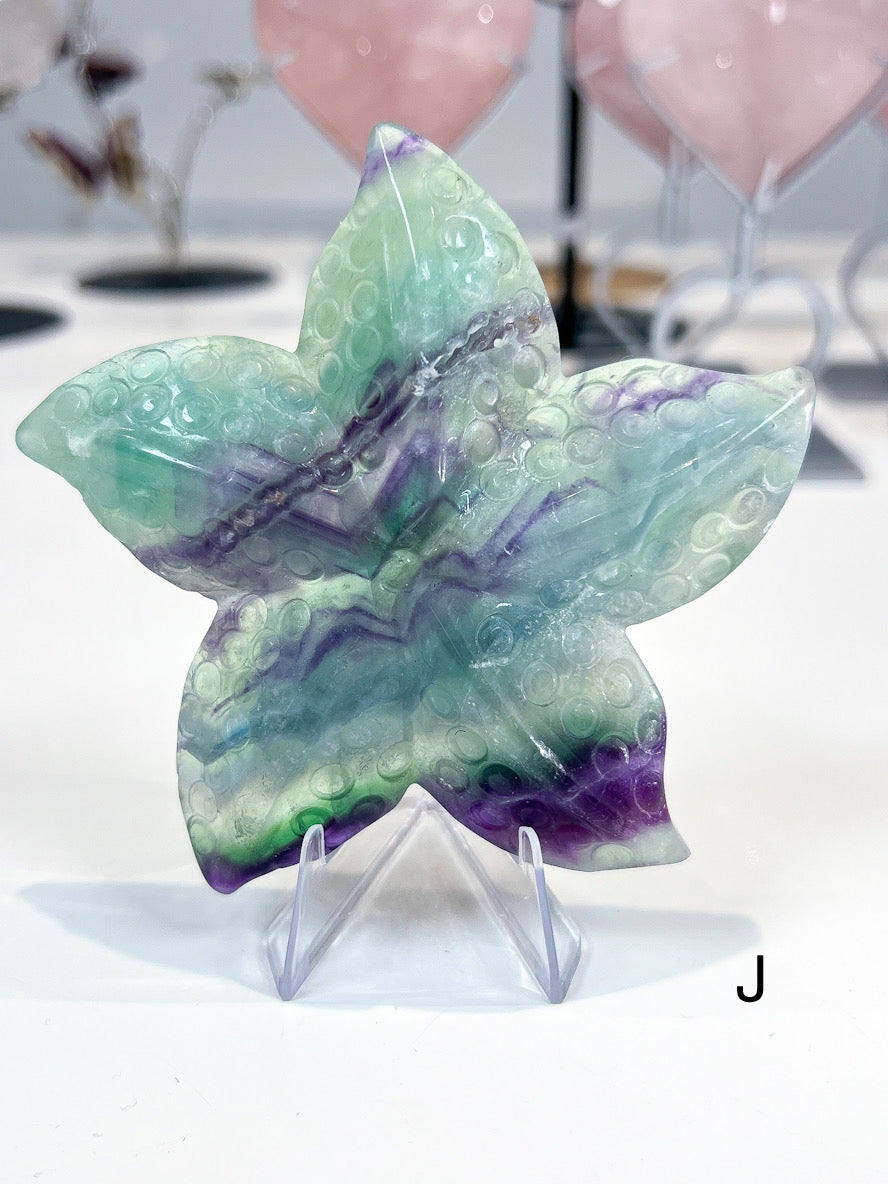 Starfish-shaped green and purple crystal on a stand with blurred background