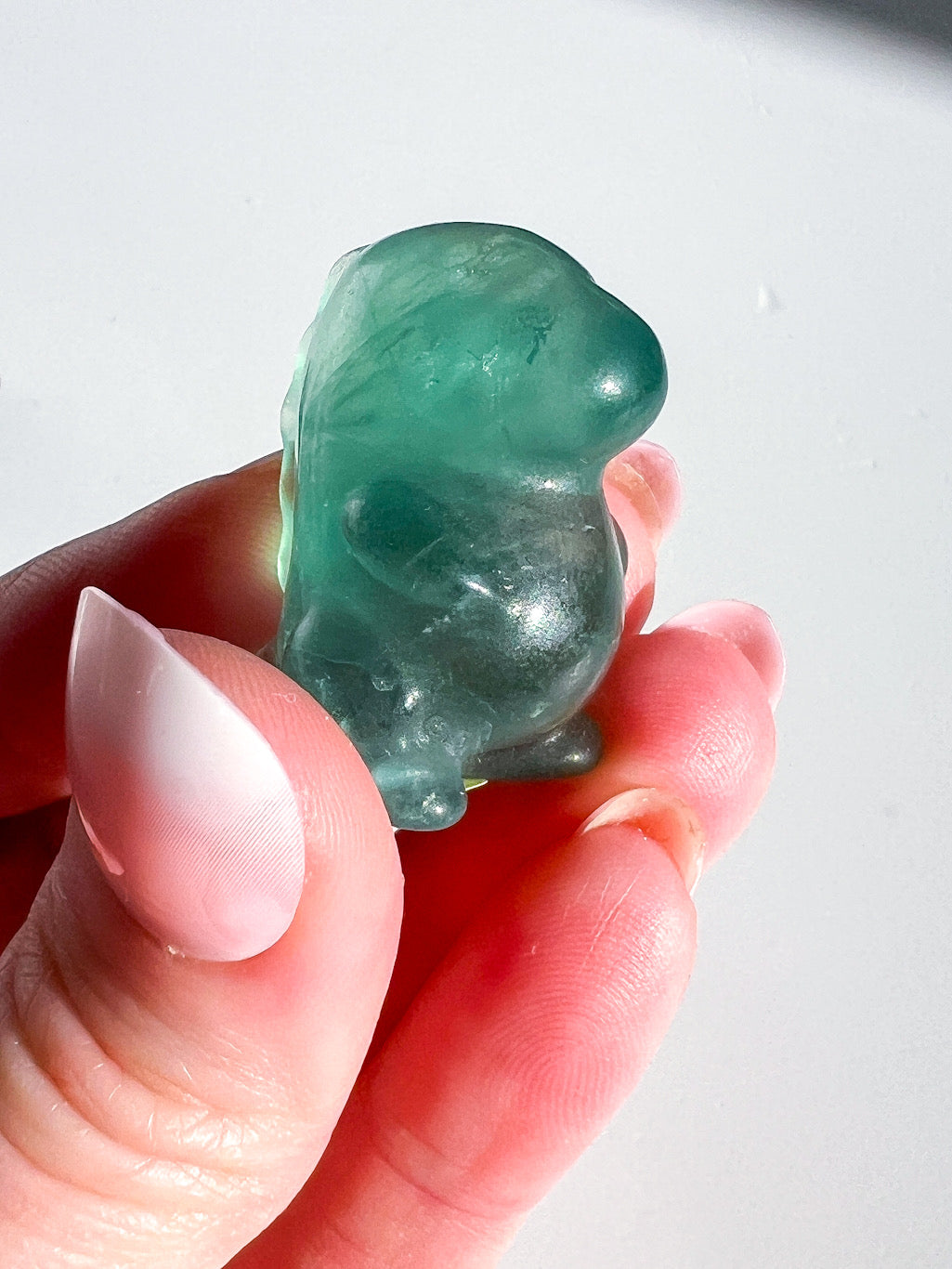 Green crystal dinosaur held between fingers against a white background