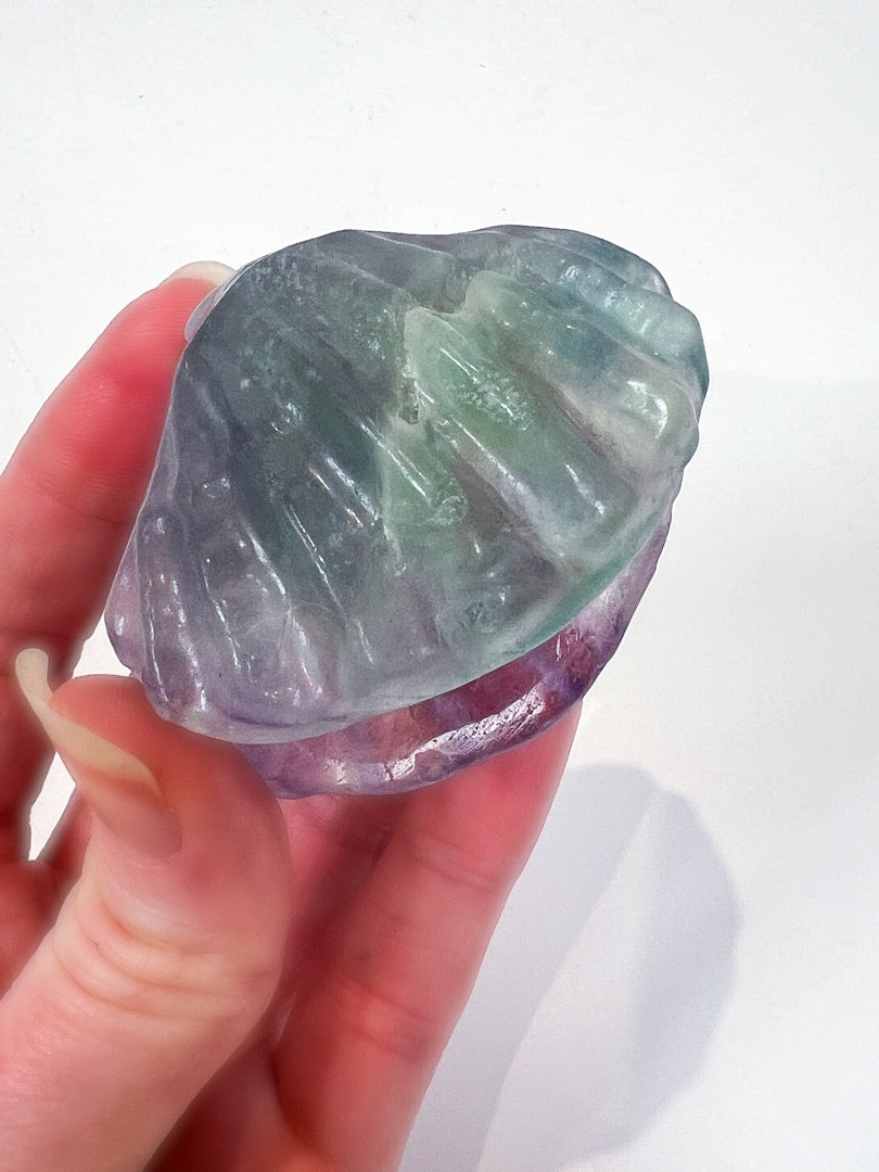 Hand holding a rough-cut gemstone with purple and green hues on a white background