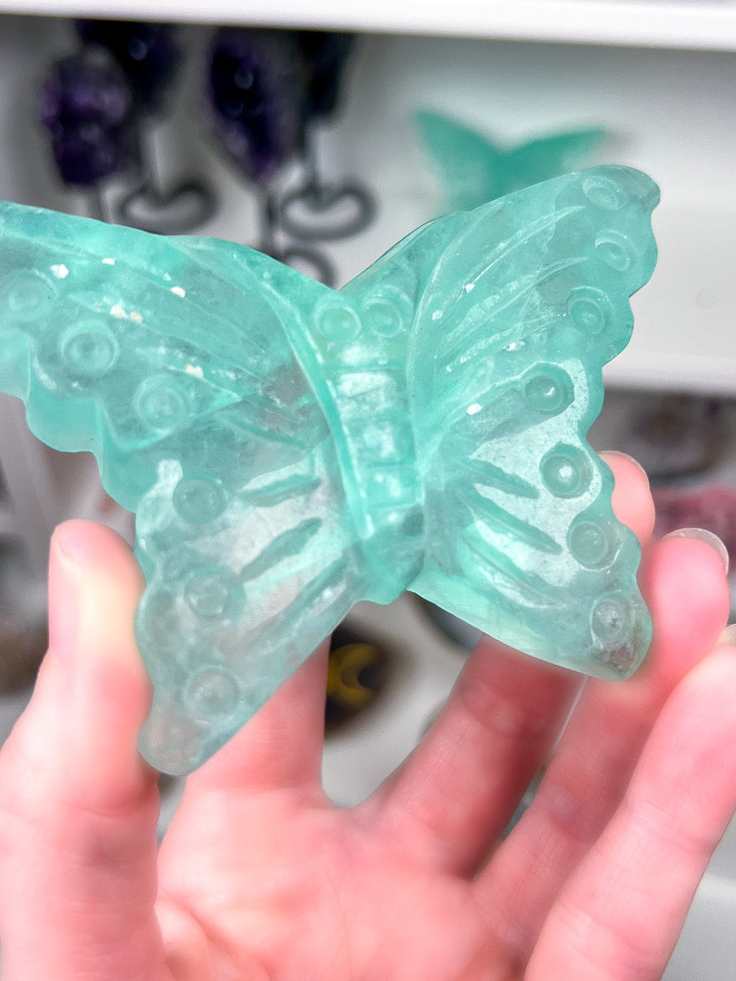 Green butterfly-shaped object held in a hand with a blurred background