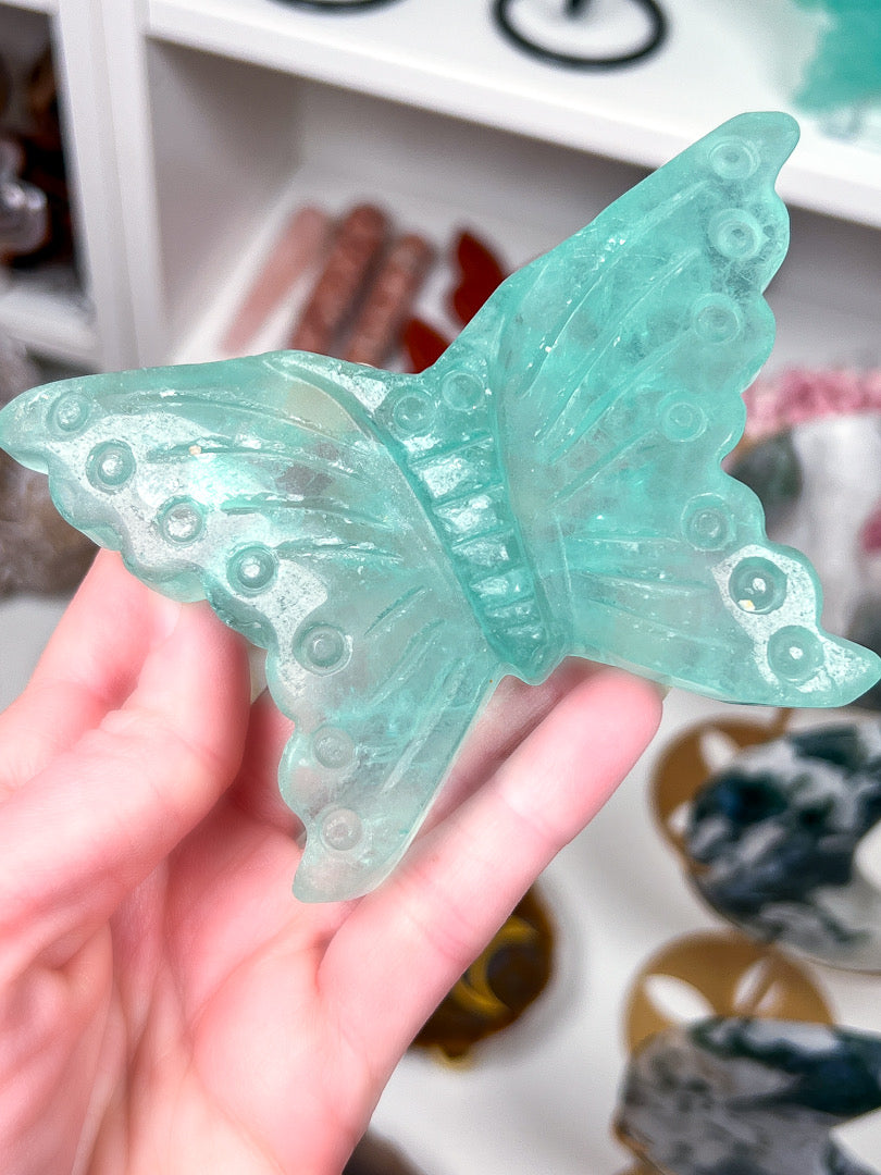 Turquoise butterfly-shaped object held in a hand with a blurred background