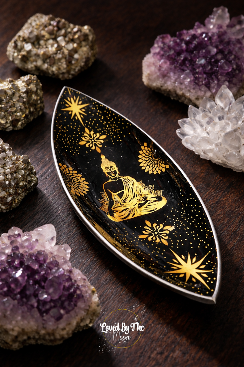 Gold and Black Buddha Incense Stick Holder on a brown wooden table surrounded by Amethyst and Clear Quartz crystals.