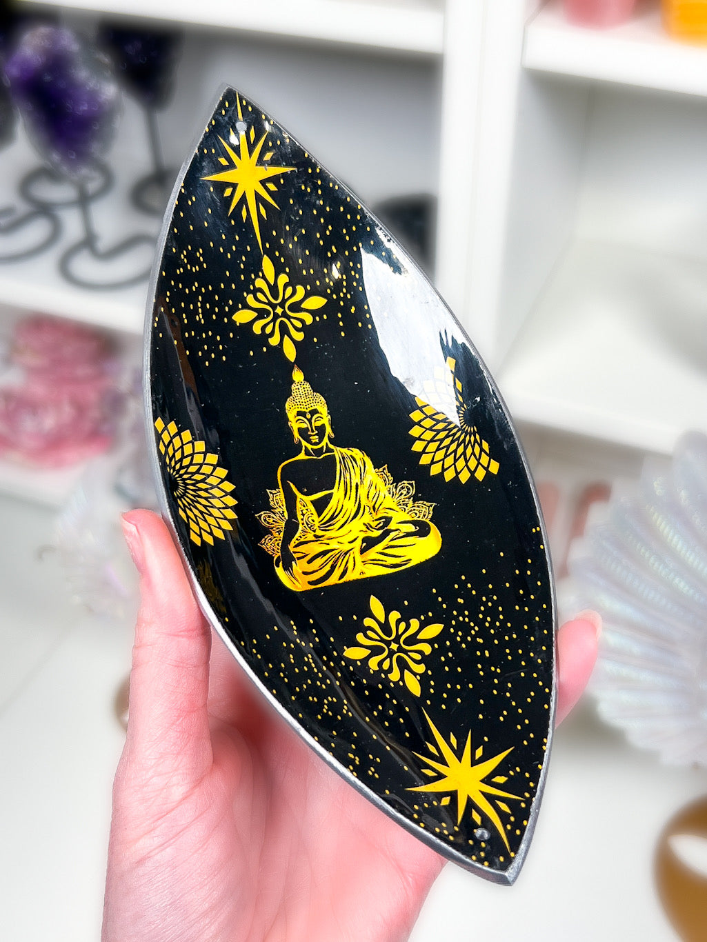 Gold and Black Buddha Incense Stick Holder in a hand with a white blurry background.