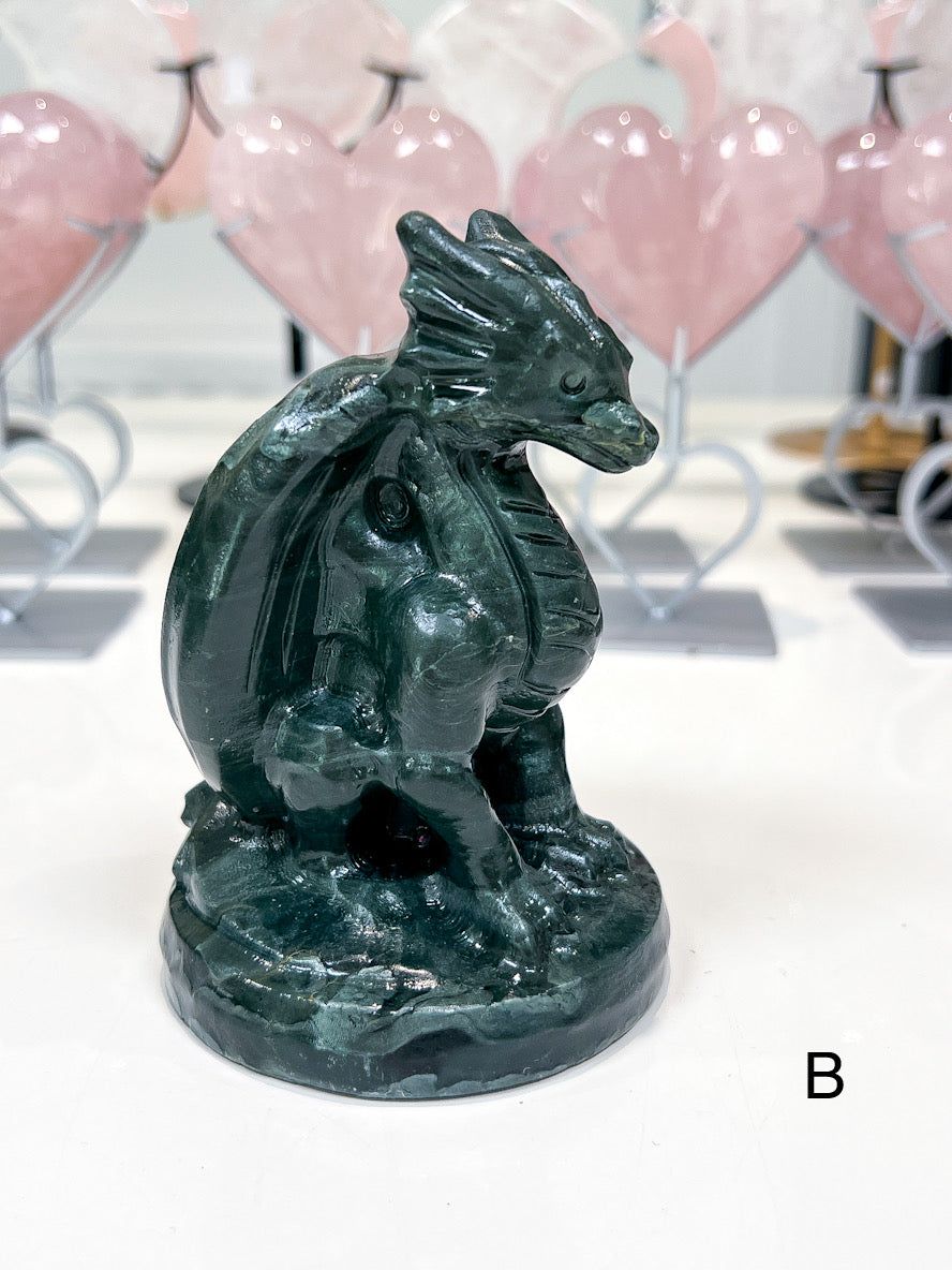 Green dragon figurine on a white surface with blurred pink heart-shaped objects in the background