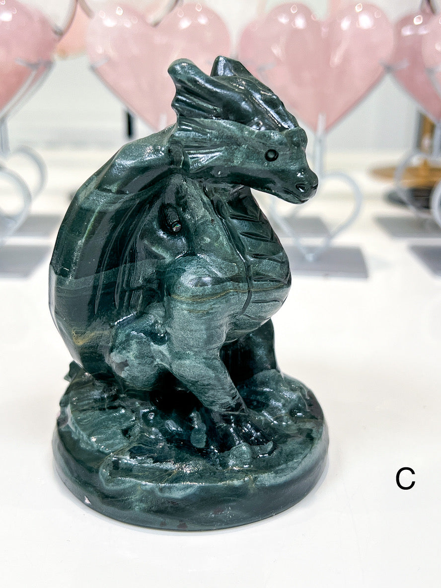 Green stone dragon figurine on a white surface with pink balloons in the background