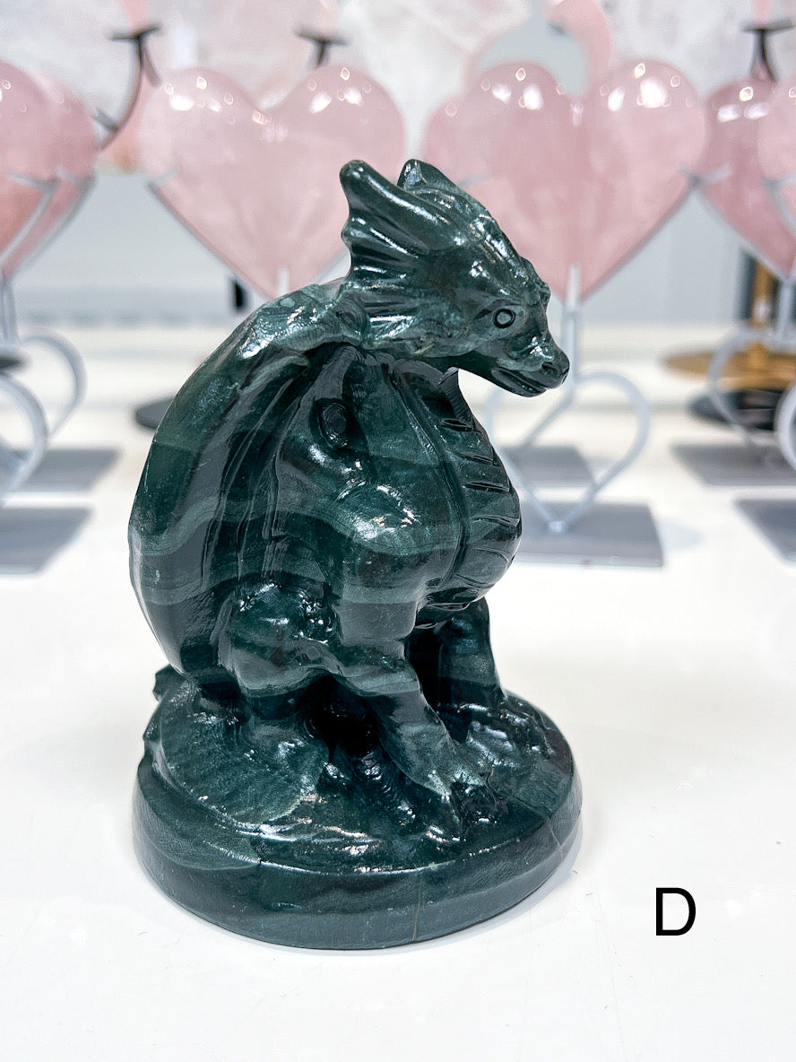 Green dragon figurine on a white surface with blurred pink heart-shaped objects in the background