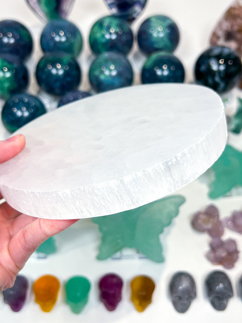 White flat crystal held over a selection of coloured stones on a white background