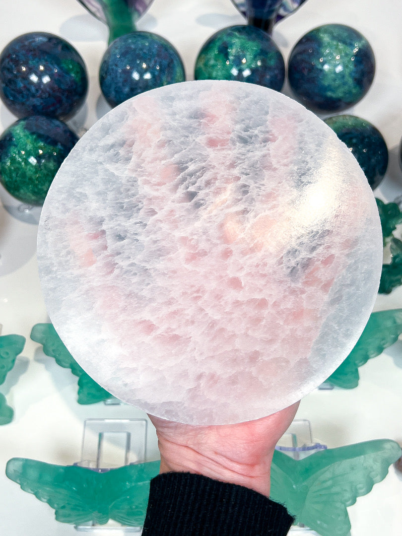 Hand holding a round, translucent crystal ball with green marbled stones in the background.