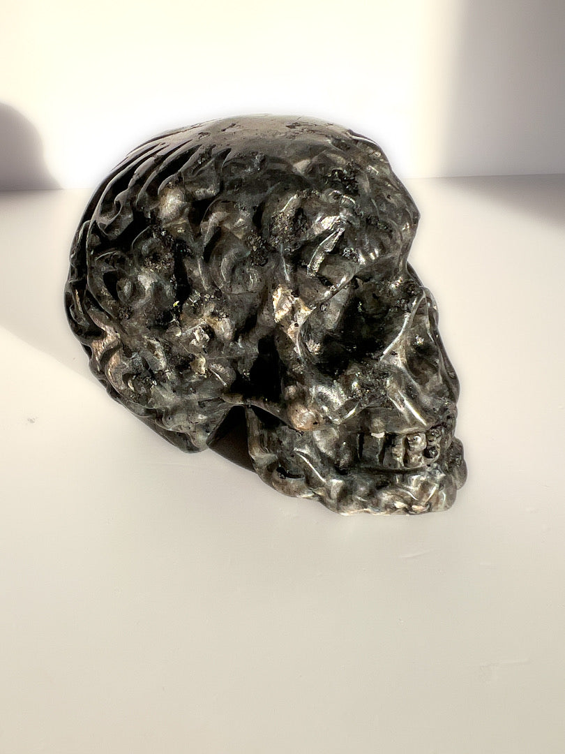 Silver skull figurine on a white surface with a blurred background