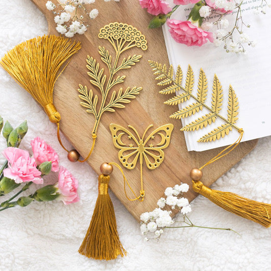 Decorative gold bookmarks with tassels on a wooden board surrounded by flowers.