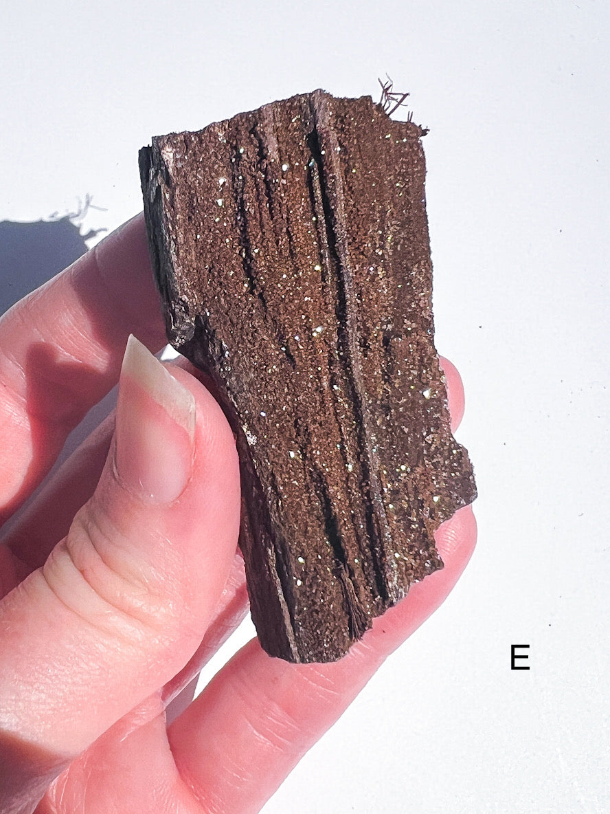 Person holding a piece of layered brown crystal mineral against a white background
