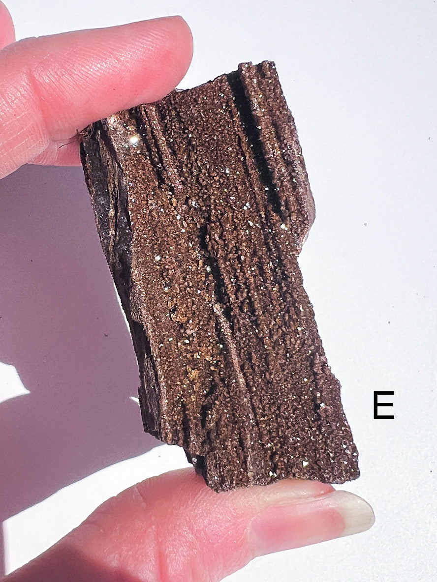 Person holding a piece of layered brown crystal mineral against a white background
