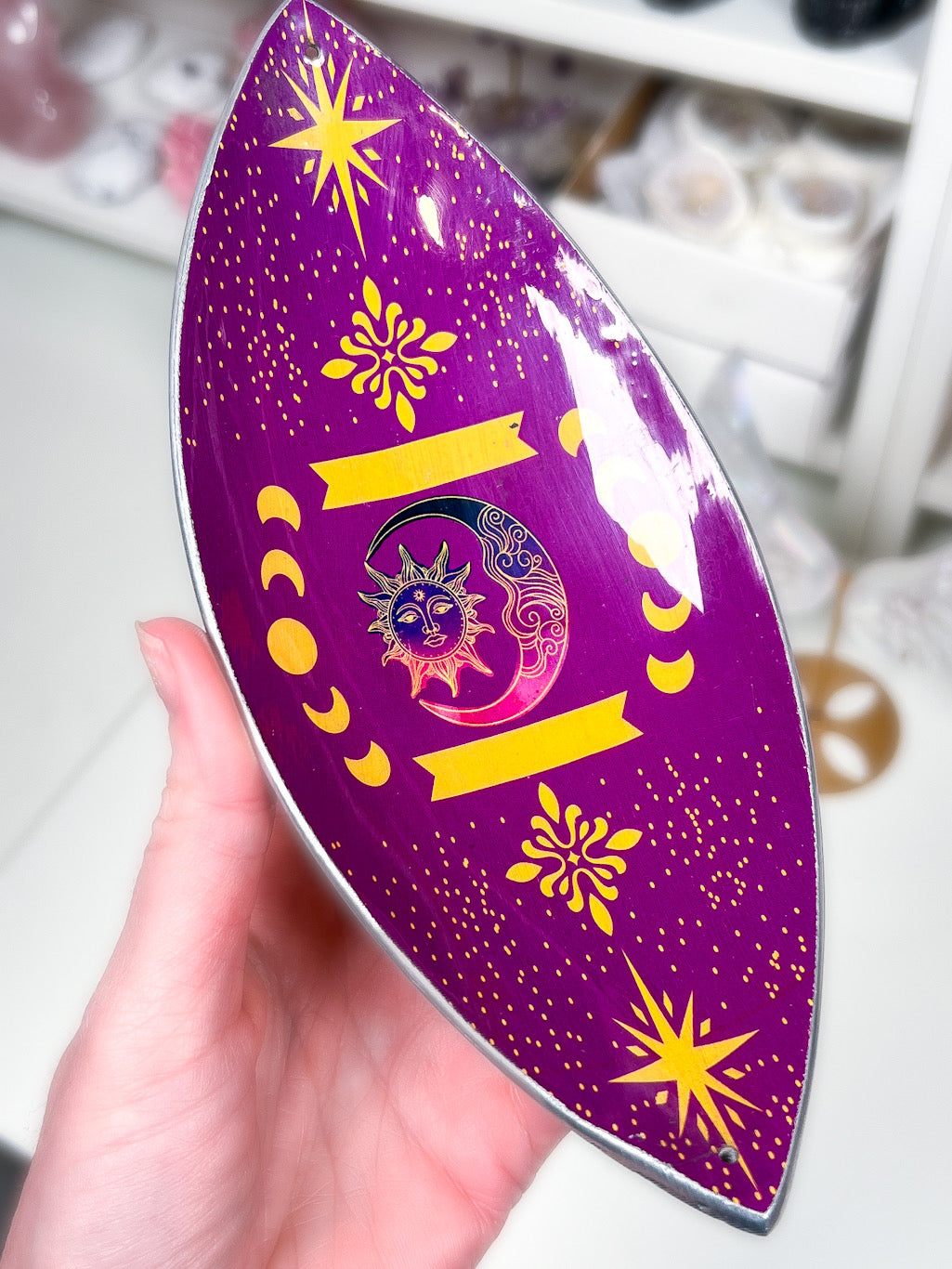 purple sun and moon phases incense stick holder in a hand with a blurry white background.
