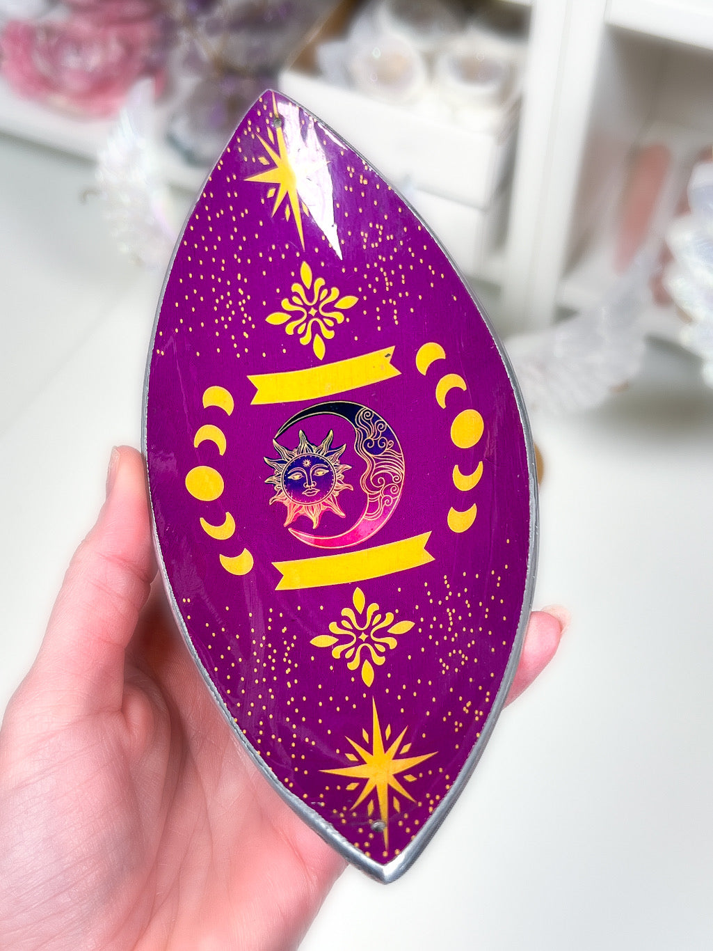 purple sun and moon phases incense stick holder in a hand with a blurry white background.