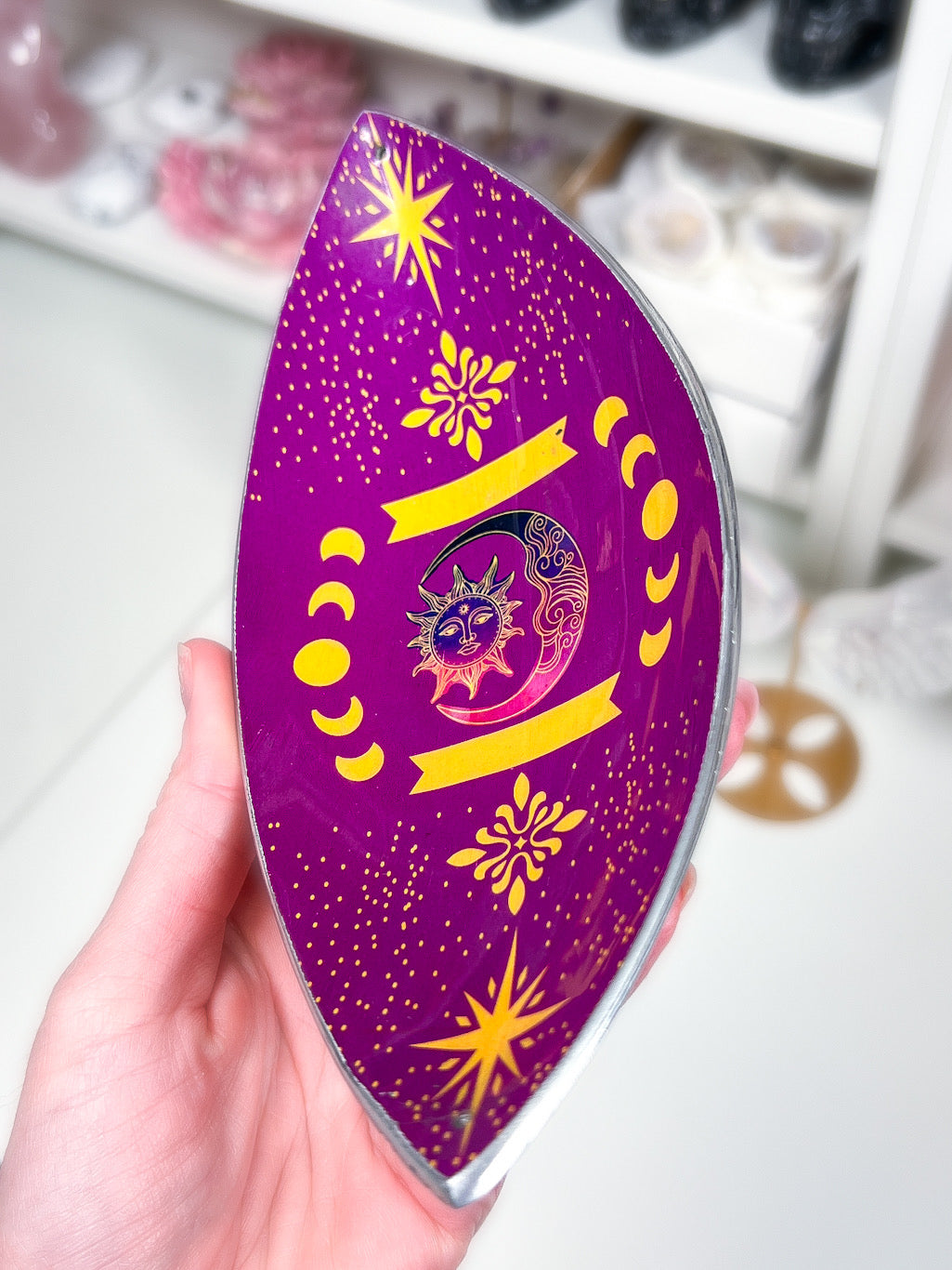 Purple sun and moon phases incense stick holder in a hand with a blurry white background.