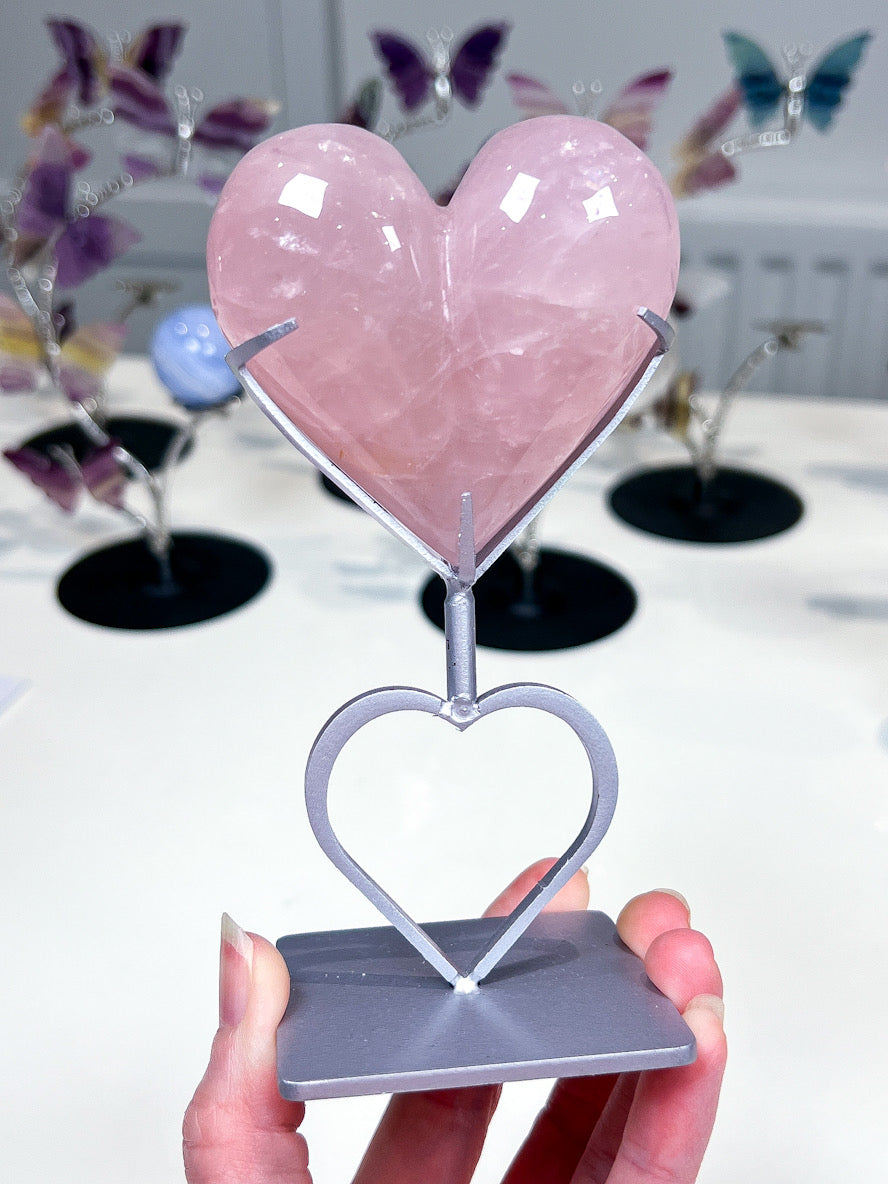 Pink crystal heart on a silver stand held by a hand with blurred butterfly decorations in the background.