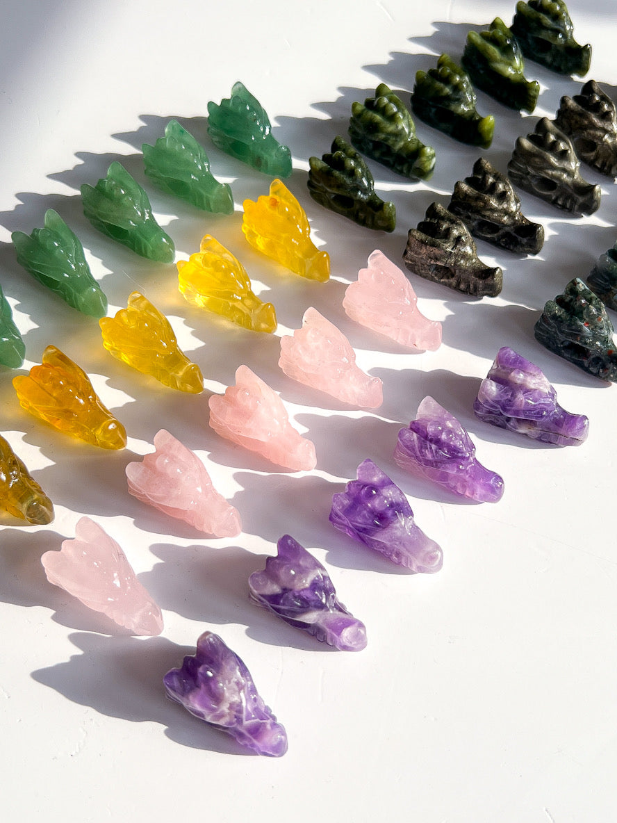 Colourful crystal-like dragon head carvings arranged on a white surface