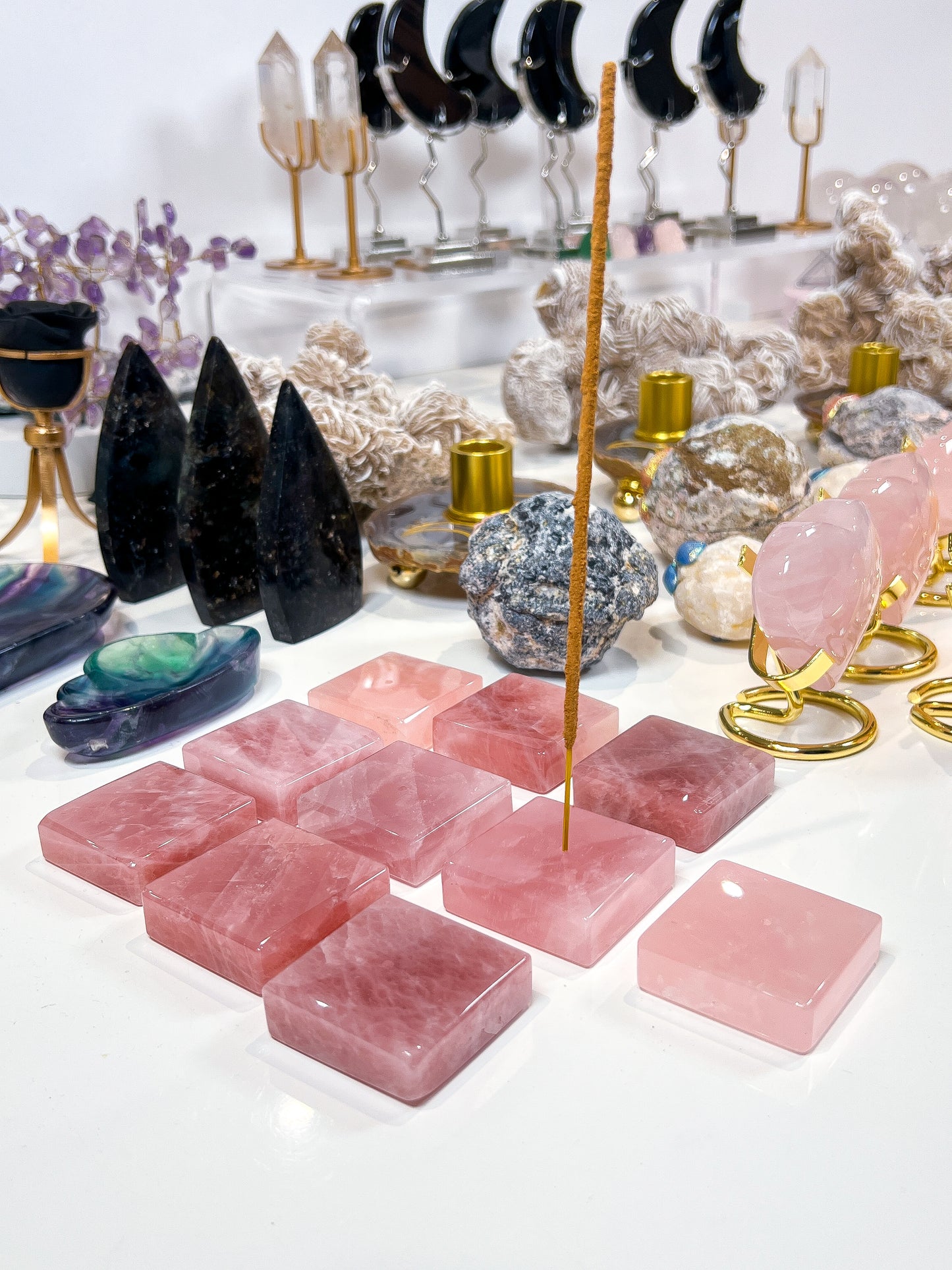 Rose Quartz incense stick holders on white table with lots of crystals in the background.
