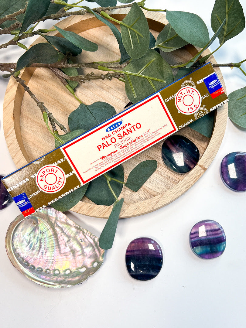 Palo Santo incense stick box on a wooden plate with green leaves and stones.