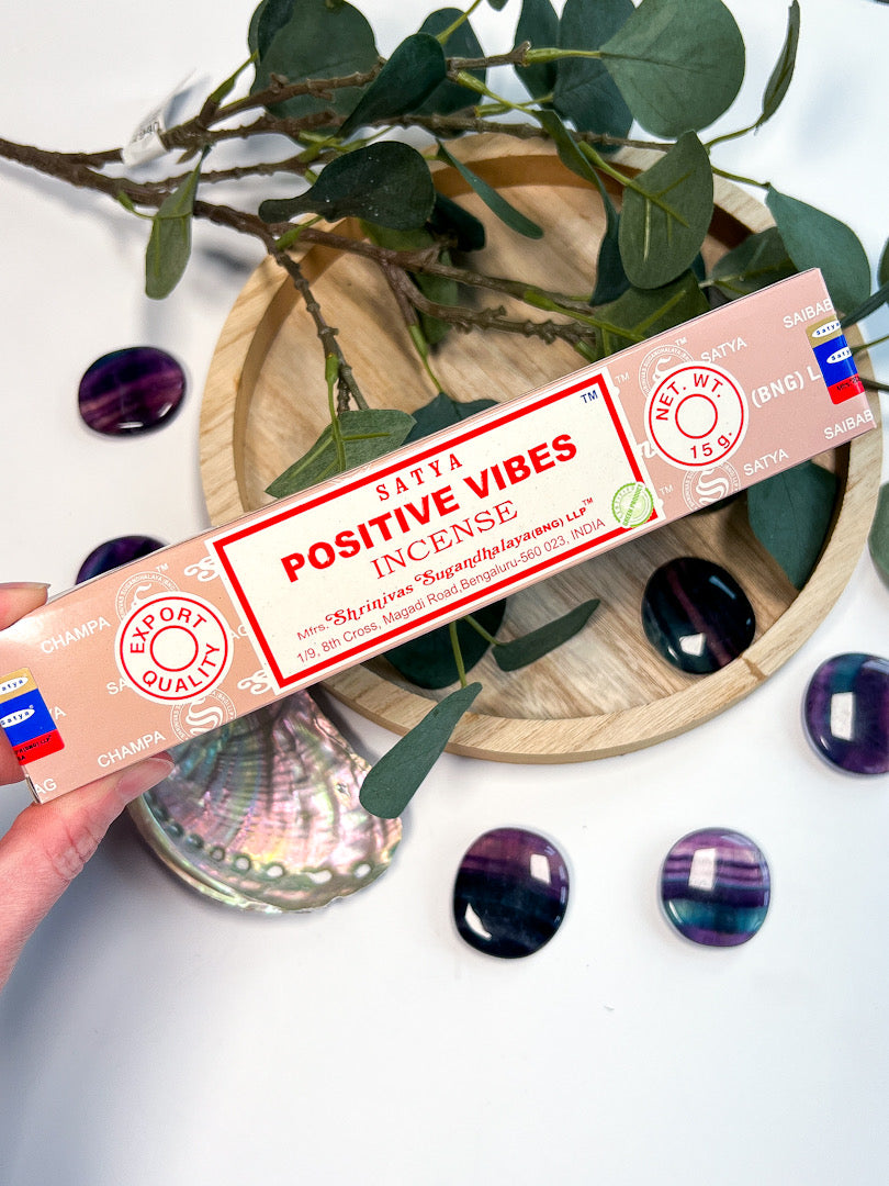 Scented incense stick packaging with 'Positive Vibes' text on a decorative background with greenery and stones.