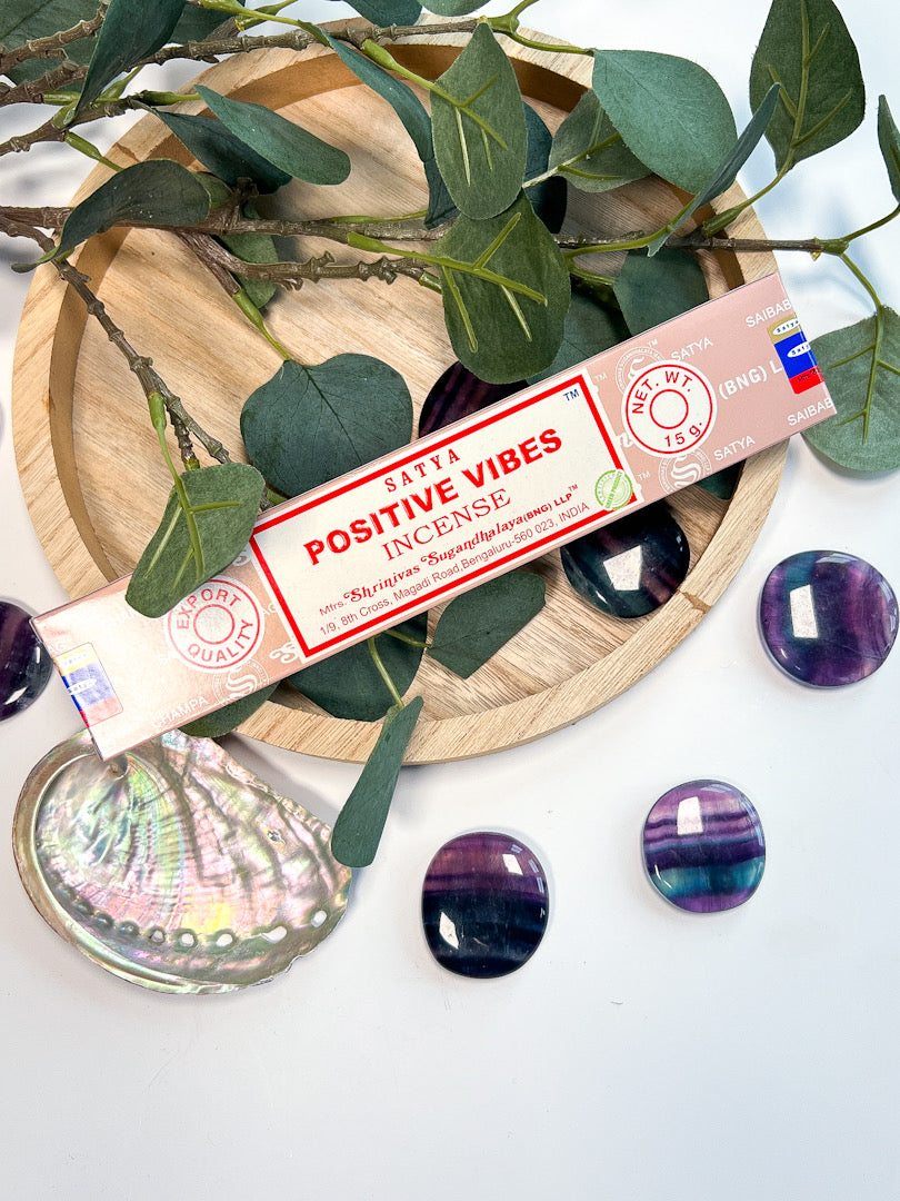 Scented stick labeled 'Positive Vibes' on a decorative plate with green leaves and purple stones.
