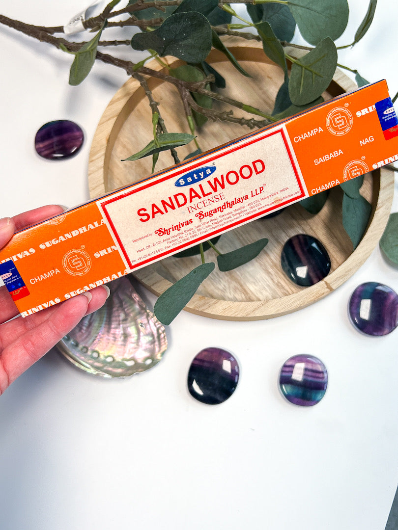 Sandalwood incense stick box held by a hand with decorative stones and leaves in the background