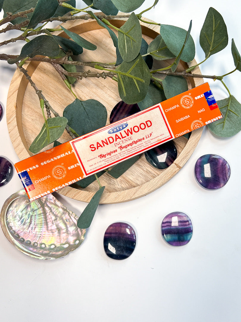 Sandalwood incense stick box on a decorative plate with green leaves and purple stones.