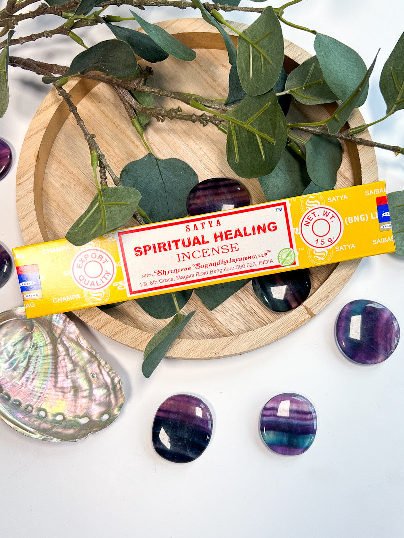 Satya Spiritual Healing Incense packaging on a wooden plate with leaves and stones.