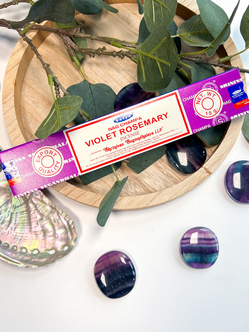 Violet Rosemary incense stick packaging on a wooden plate with green leaves and purple stones.
