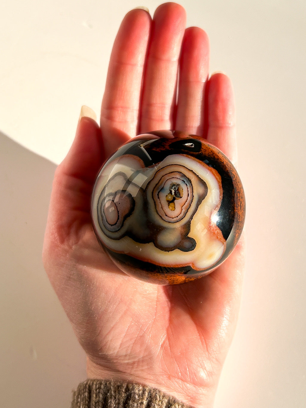 Hand holding a marbled stone with intricate patterns against a neutral background