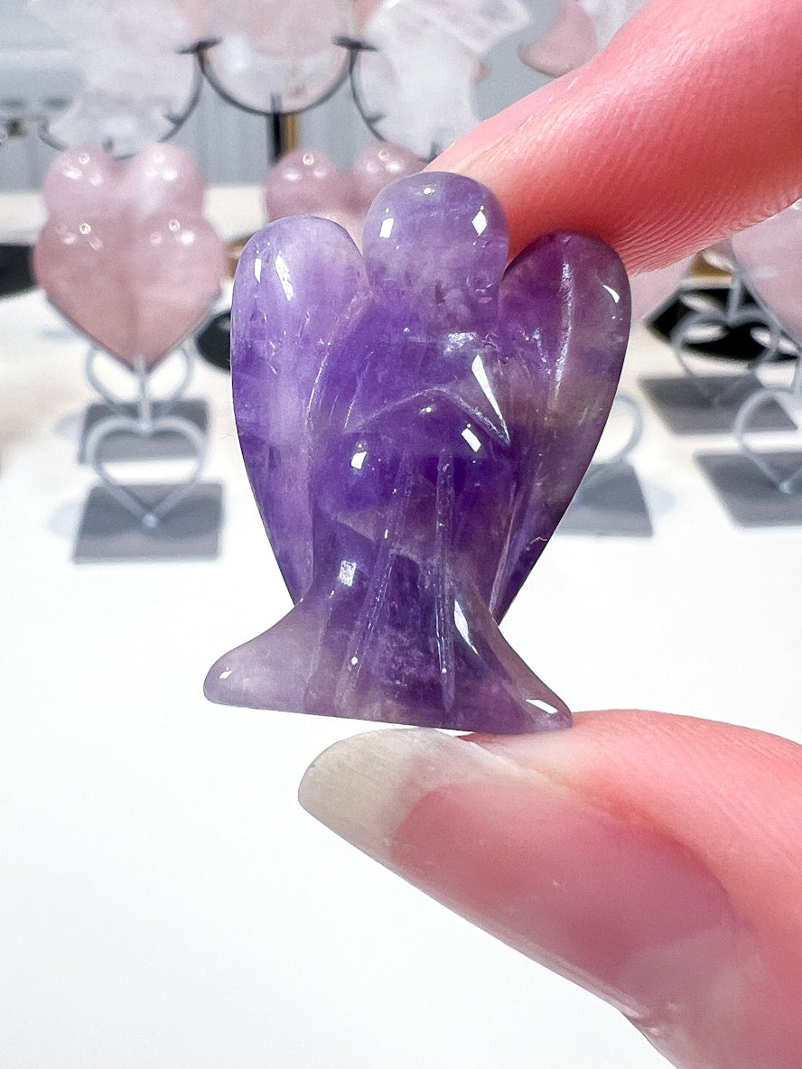 Purple crystal angel figurine held between fingers with blurred background